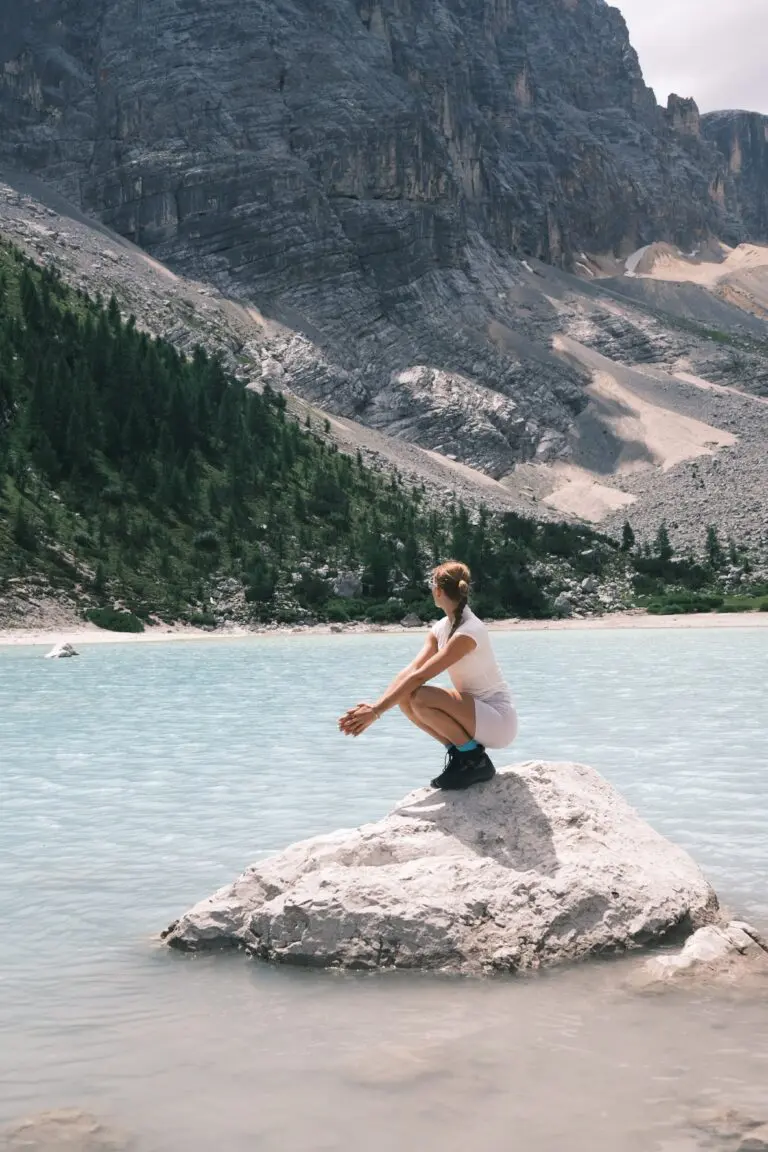 Frau sitzt auf einem Felsen an einem türkisfarbenen Bergsee in den Dolomiten, Italien